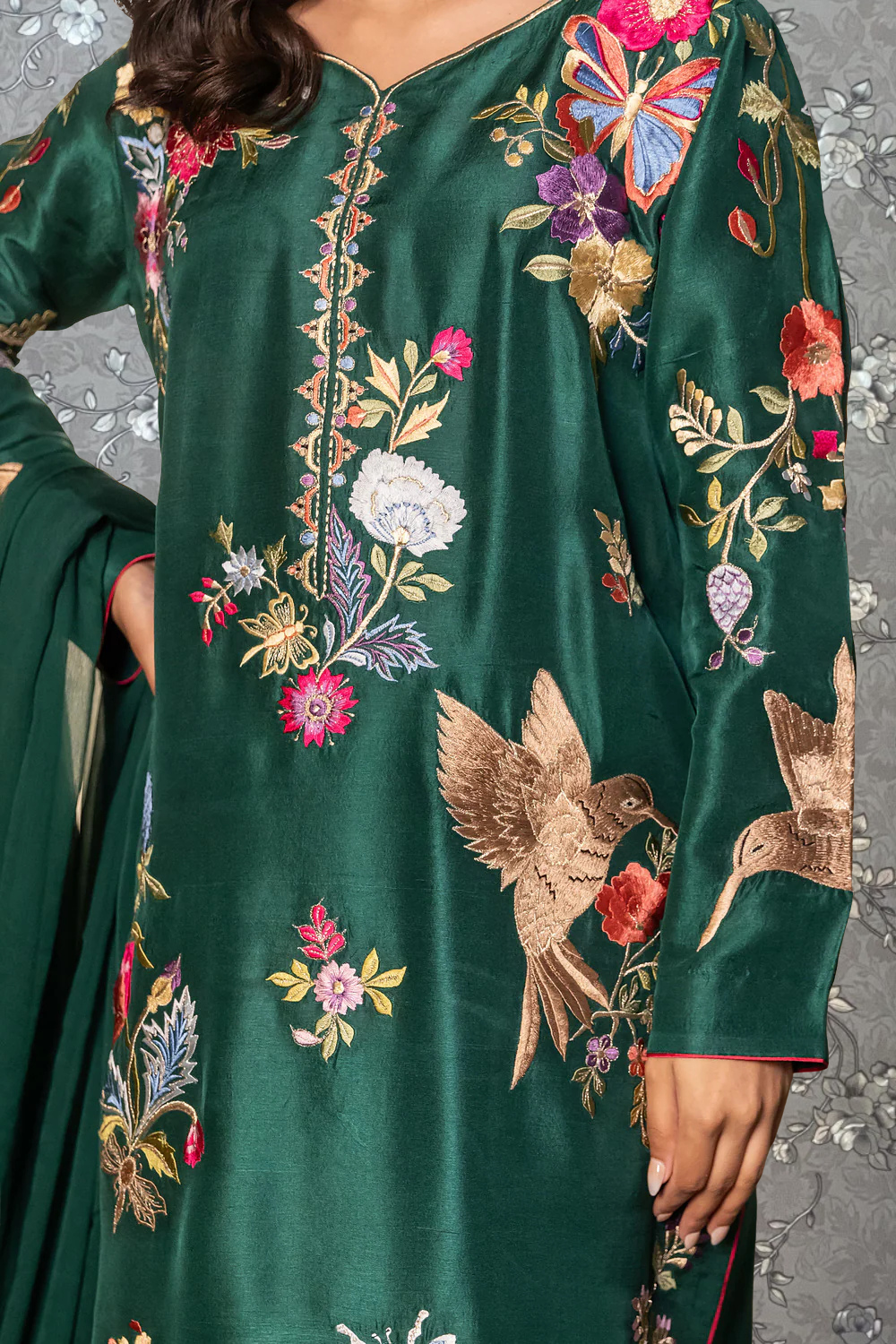 A close-up of a woman wearing a green dress with intricate embroidered designs, including flowers and birds.
