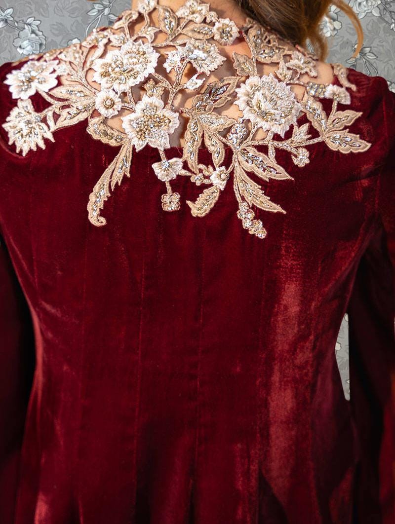 a close-up view of a person wearing a red velvet jacket with intricate embroidered floral designs on the back.