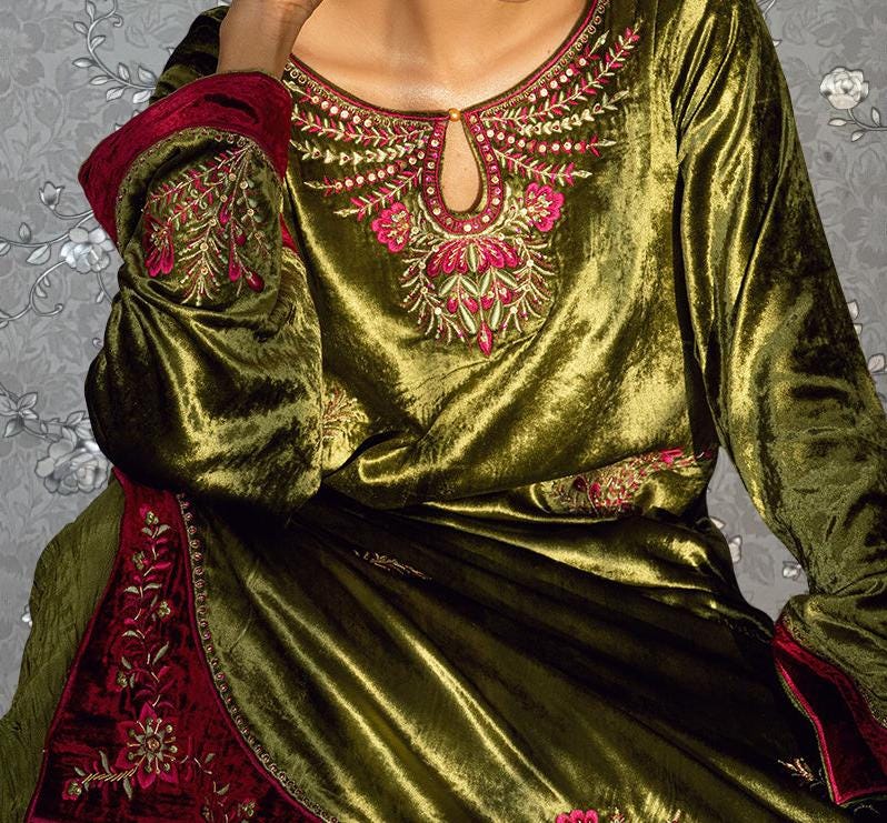 A close-up view of a person wearing a green velvet dress with intricate embroidered patterns in red and gold.