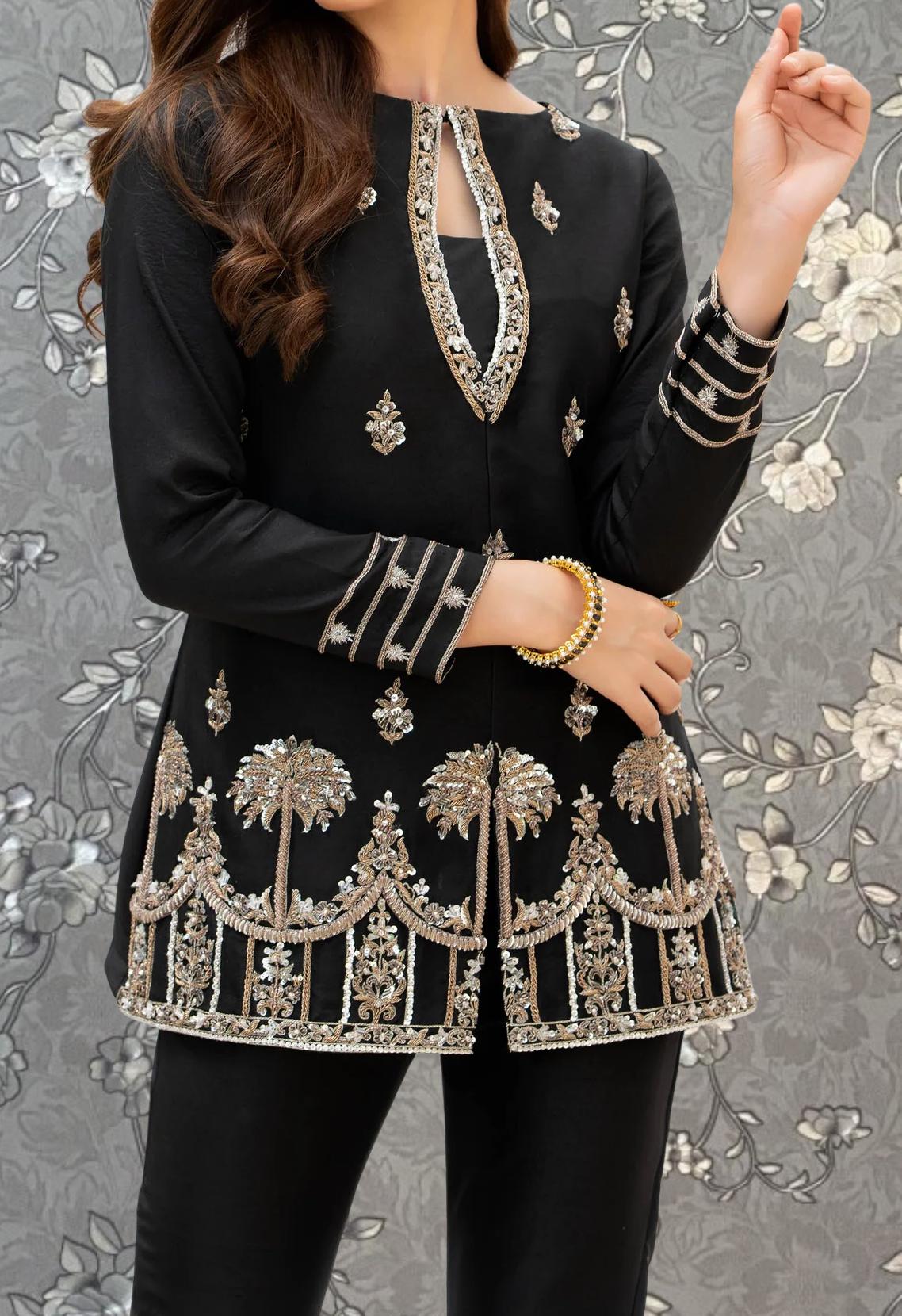 A woman wearing a black dress with intricate gold embroidery and patterns, posing with her hand raised.