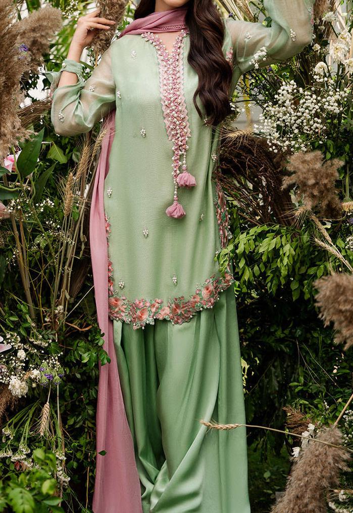 A woman wearing a green dress with pink accents and floral designs, standing in a lush, green garden setting.