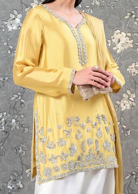 A woman wearing a yellow dress with intricate silver embroidery and holding a small clutch purse.