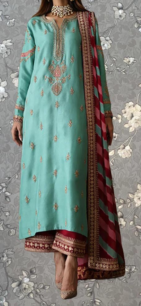 A woman wearing a long, turquoise-colored dress with intricate embroidery and a matching red and gold shawl.