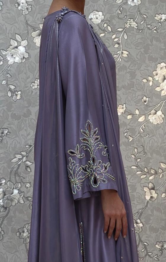 A person wearing a long, purple dress with intricate embroidered designs on the sleeves and hem.