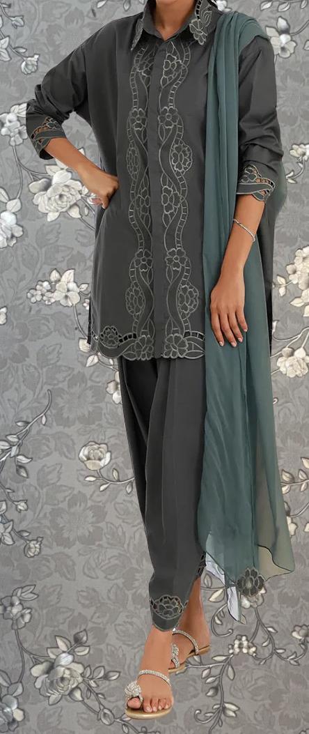 A person wearing a gray dress with intricate embroidery and a matching green shawl, standing against a gray floral background.