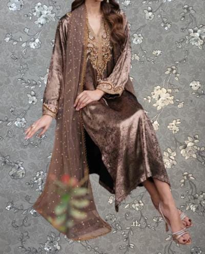 A woman wearing a long, brown dress with gold embroidery and a matching shawl is shown against a gray floral background.