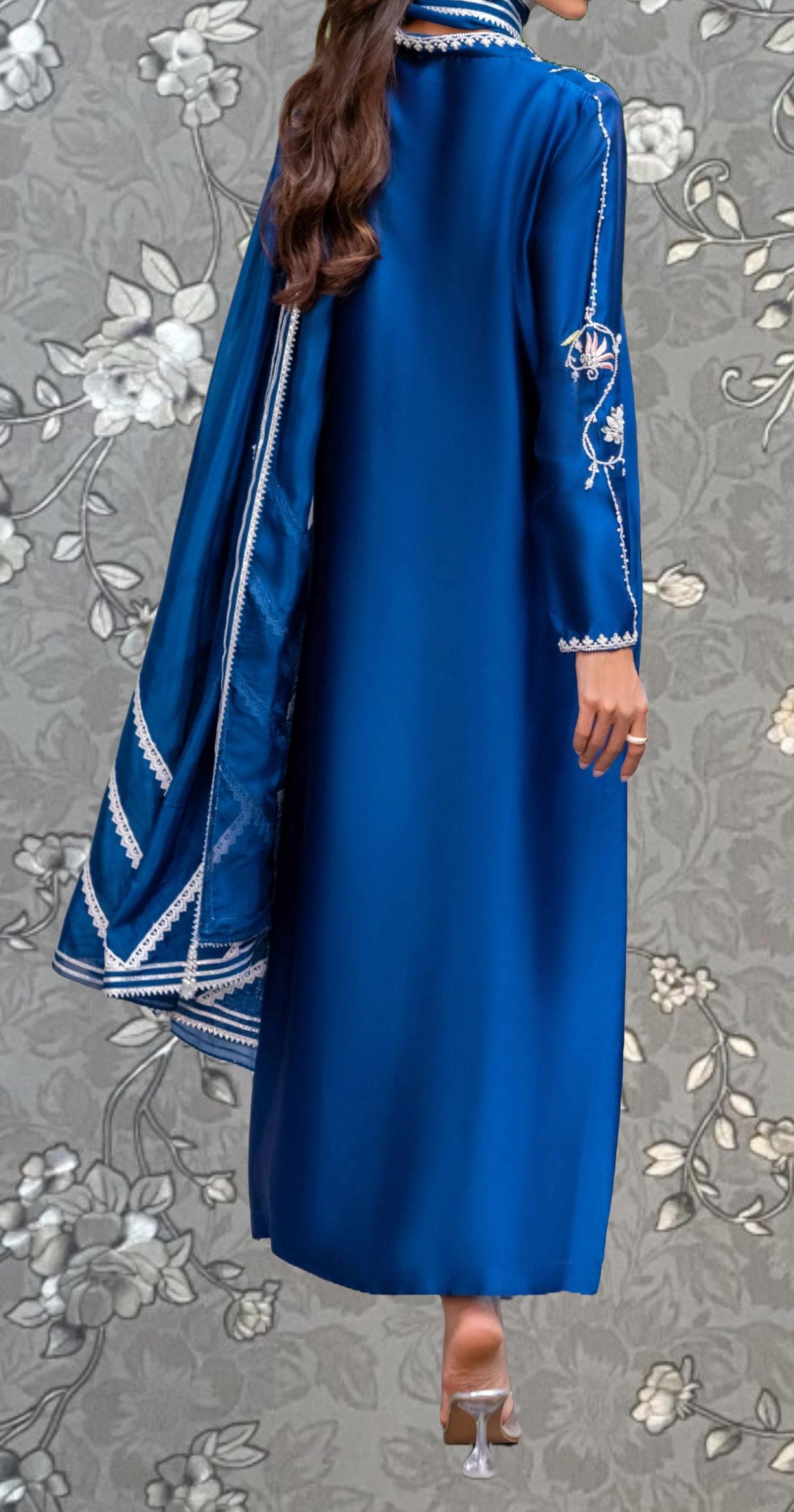 A woman wearing a long, blue dress with white embroidered patterns on the sleeves and a matching blue shawl draped over her shoulders.