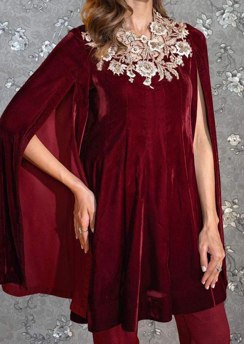 A woman wearing a burgundy velvet dress with a floral embroidered collar and cape-like sleeves.