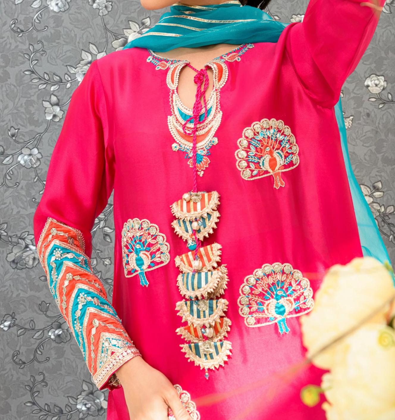 A close-up of a person wearing a bright pink dress with intricate embroidery and colorful patterns.