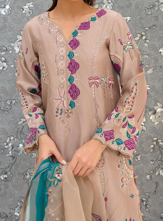 A woman wearing a beige dress with intricate floral embroidery stands against a gray floral background.