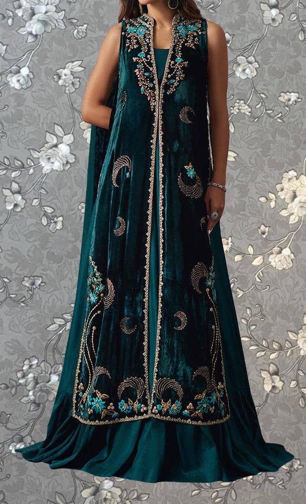 A woman wearing a long, sleeveless green velvet dress with intricate embroidered patterns.