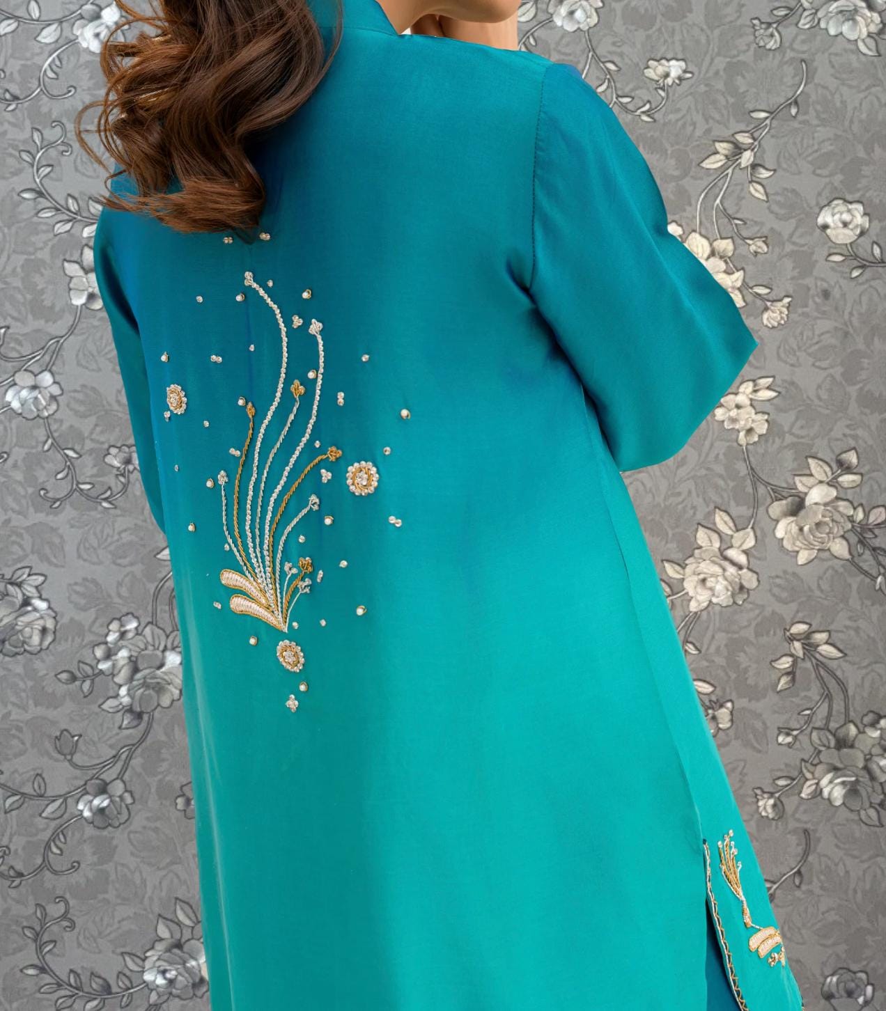 A close-up view of a person wearing a teal-colored dress with intricate embroidered designs on the back.