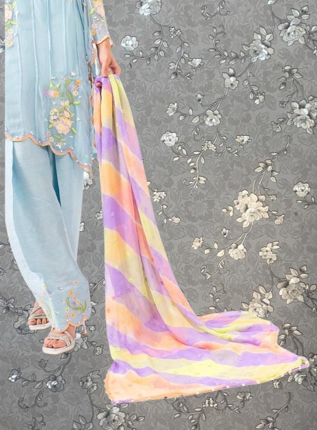 A person wearing a light blue dress with floral embroidery is holding a colorful scarf with stripes in front of a gray floral background.