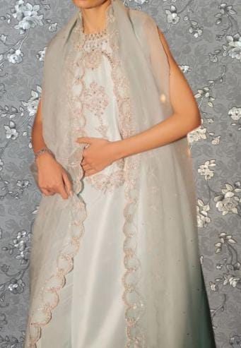 A woman wearing a long, white dress with intricate lace details and a matching shawl.