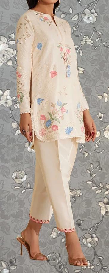A woman wearing a white dress with floral embroidery and high heels, standing against a gray floral background.