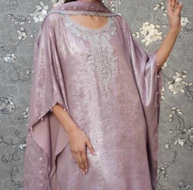 A woman wearing a long, flowing purple dress with a high collar and intricate embroidery stands against a gray floral background.