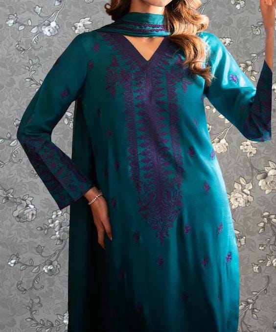 A woman wearing a teal and purple patterned dress with a high neckline and long sleeves, posing against a gray floral background.