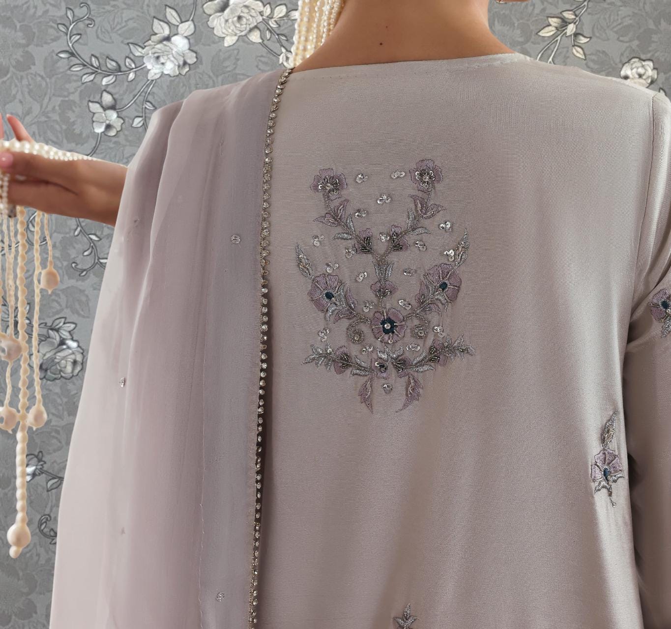 a close-up view of a person's back, wearing a grey dress with a floral embroidered design on the back.