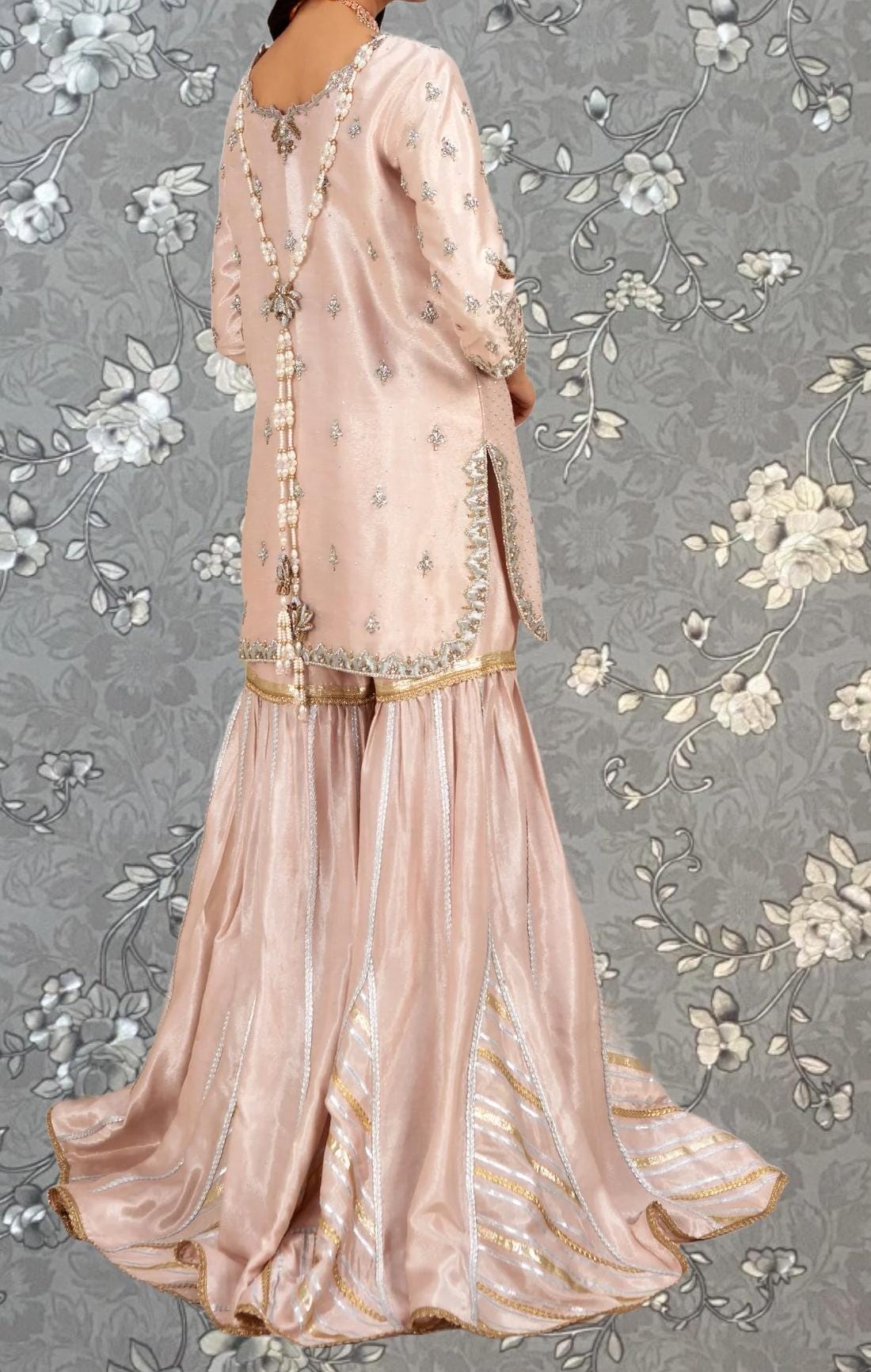 A woman wearing a long, pink dress with intricate embroidery and a high slit on the back.