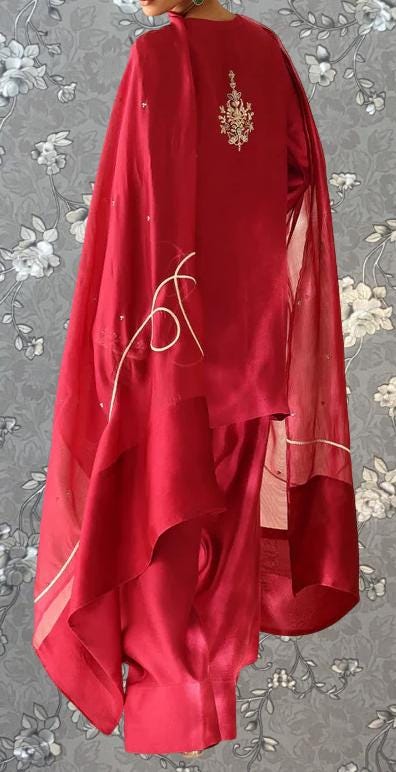 A person wearing a red dress with a floral pattern on the back, standing against a gray floral background.
