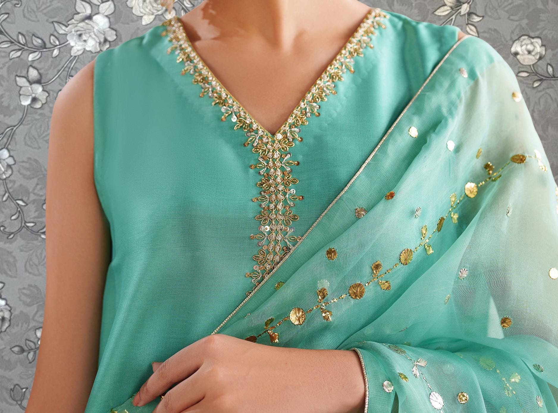 A close-up of a person wearing a turquoise dress with a gold and green embroidered design on the neckline.