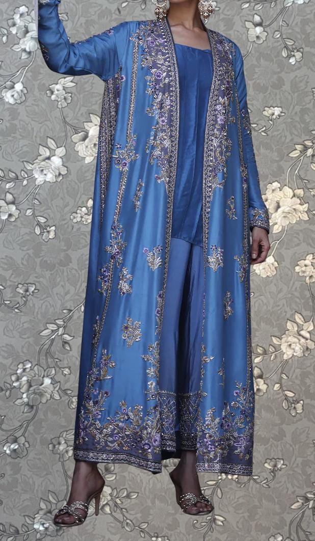 A woman wearing a long, blue dress with intricate embroidery and a matching blue jacket.