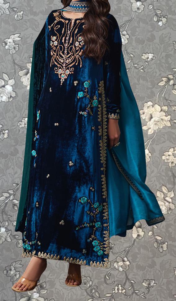 A woman wearing a long, blue velvet dress with intricate gold embroidery and floral designs.