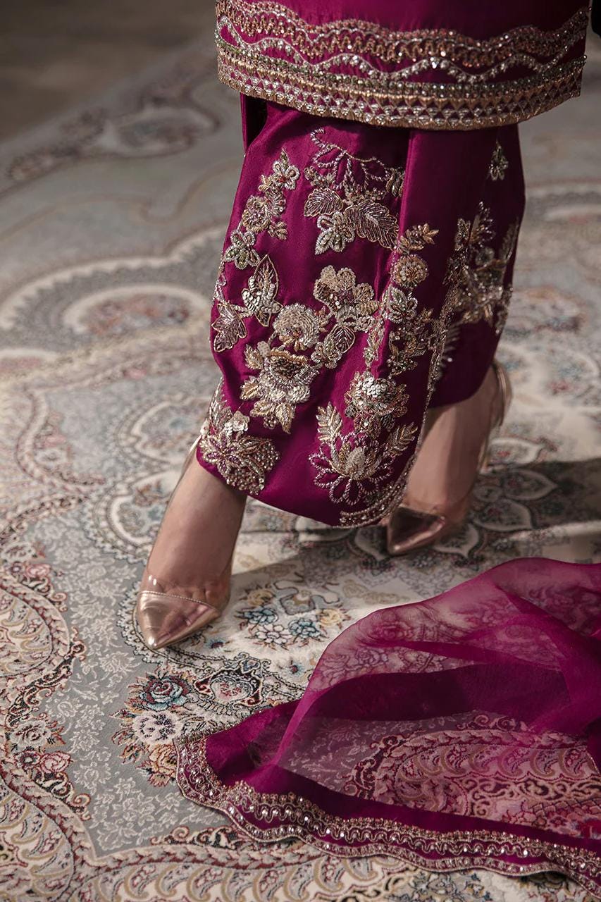 A close-up of a person wearing a vibrant purple and gold dress with intricate embroidery, standing on a patterned rug.