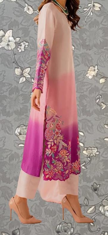 A woman wearing a long, pink and white dress with floral embroidery, standing against a gray floral background.