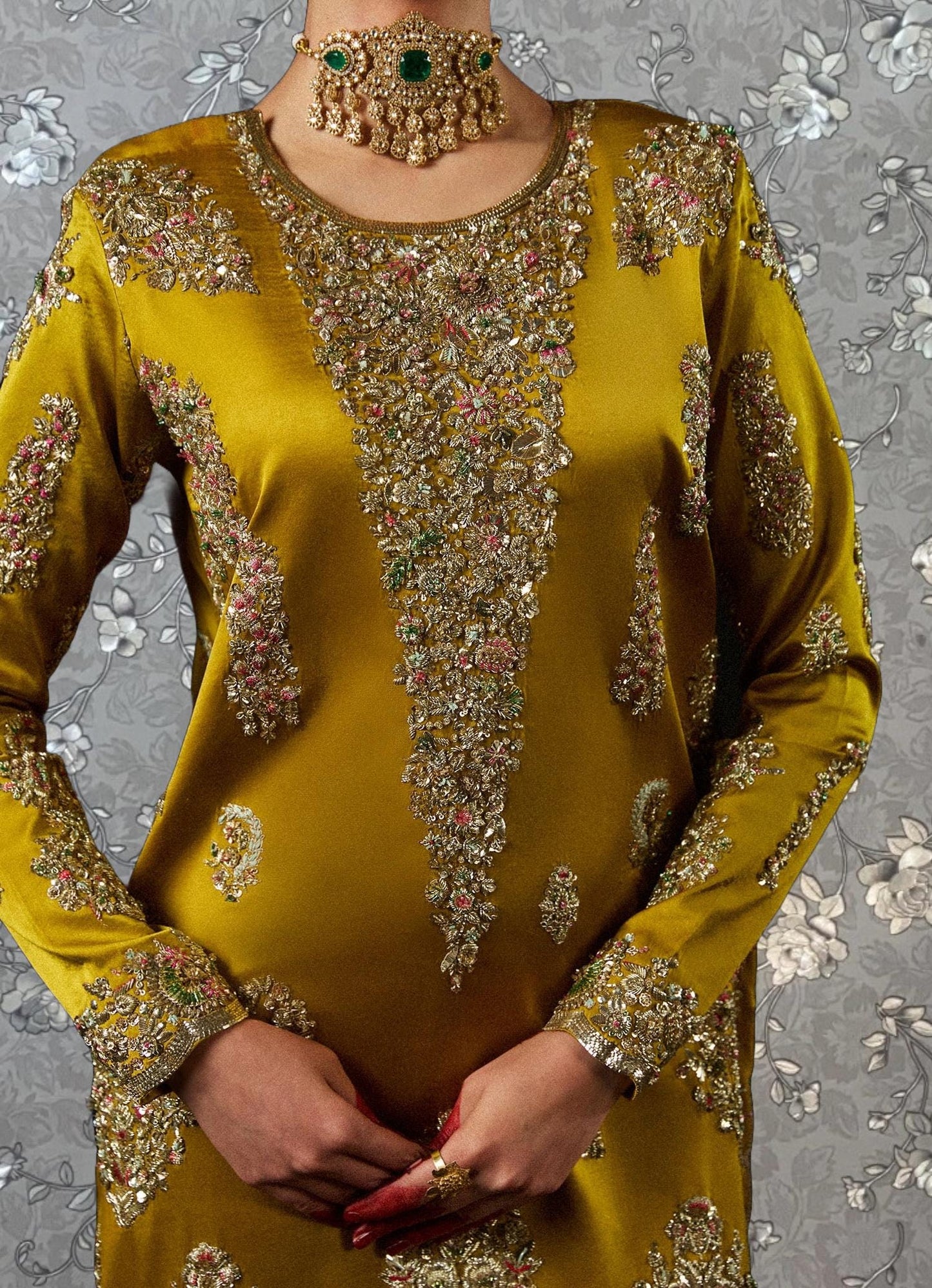 A woman wearing a gold and green embroidered dress with a large, ornate necklace.