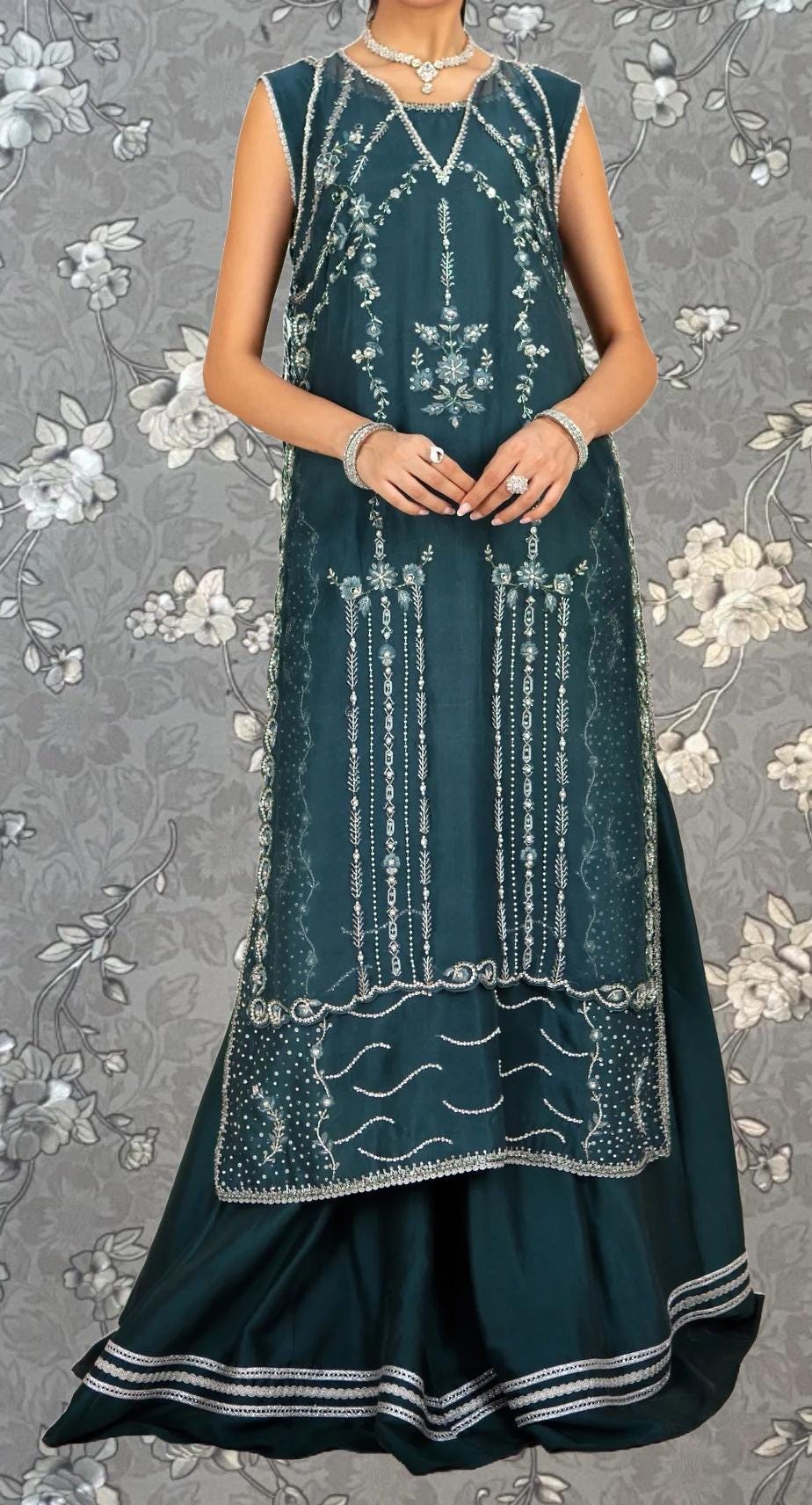 A woman wearing a sleeveless green dress with intricate embroidery and a matching skirt.