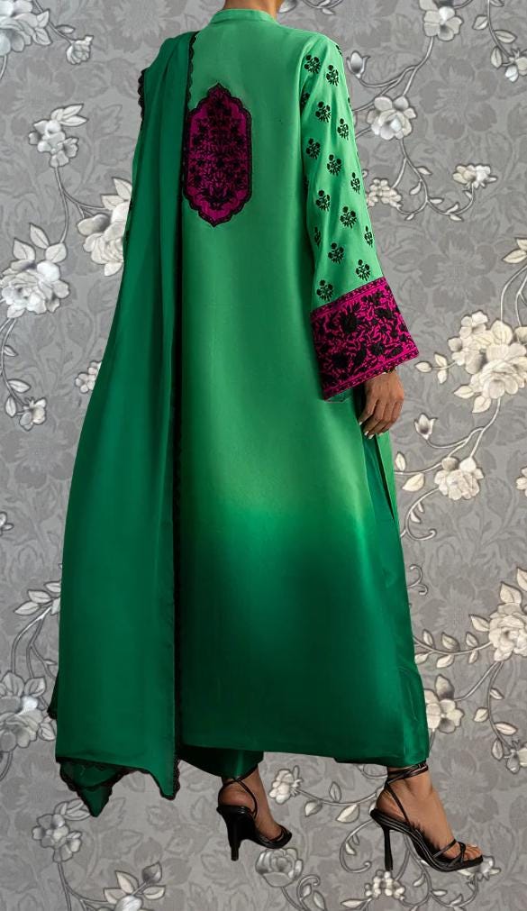 a person wearing a long green dress with pink accents, standing against a gray floral background.