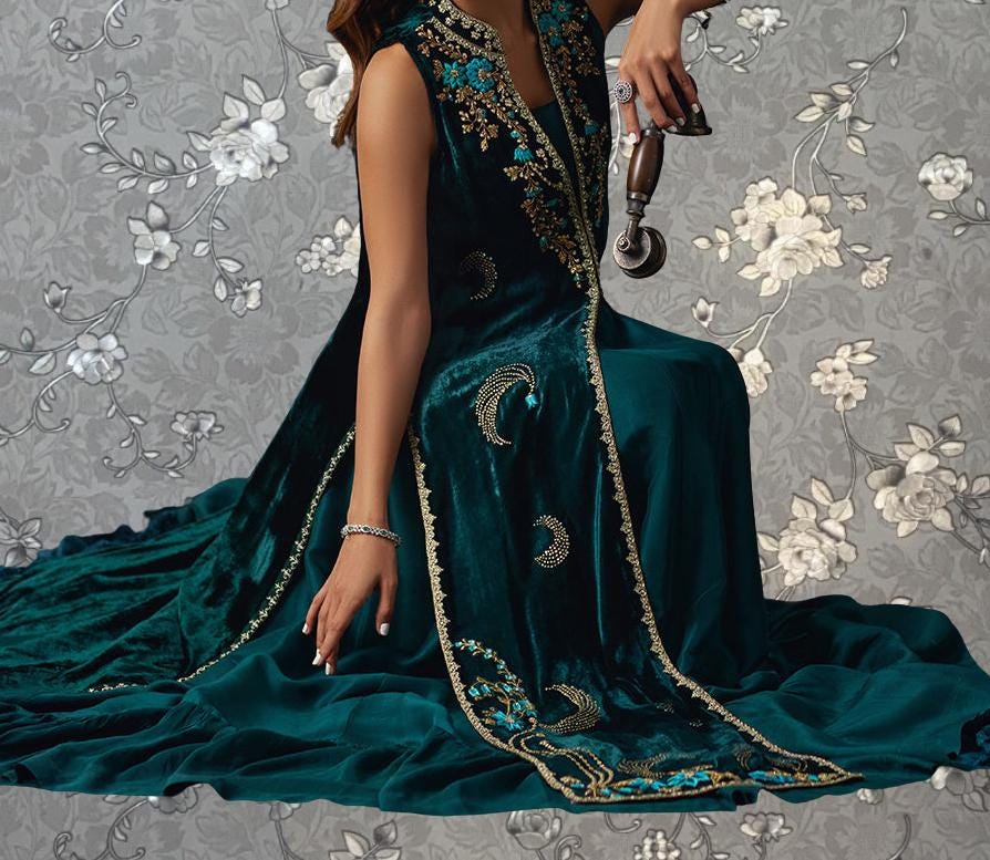 A woman in a green and gold dress is sitting on a floral patterned surface, holding a small object in her hand.