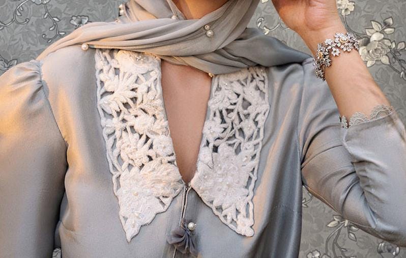 A close-up of a person wearing a gray dress with lace detailing and a scarf, posing against a floral background.