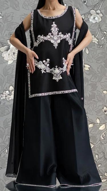A woman wearing a black dress with intricate embroidery and a black shawl draped over her shoulders.