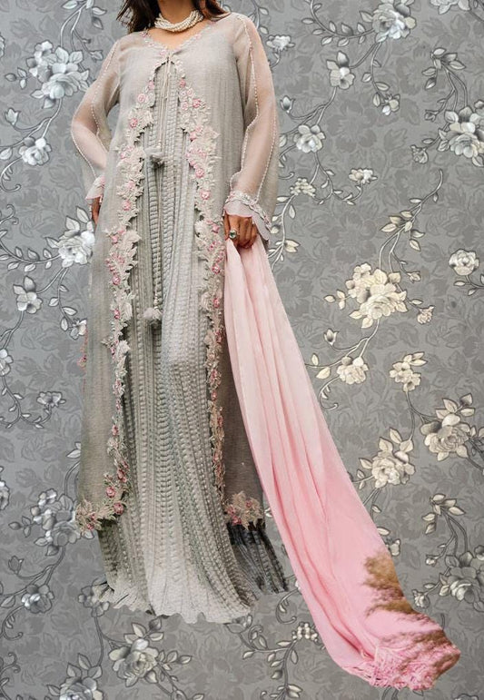 A woman wearing a long, gray dress with intricate floral embroidery and a pink shawl draped over her shoulders.