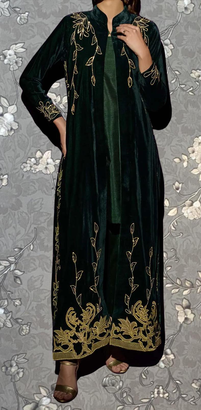 A person wearing a long, green velvet coat with gold embroidered designs on the sleeves and hem.