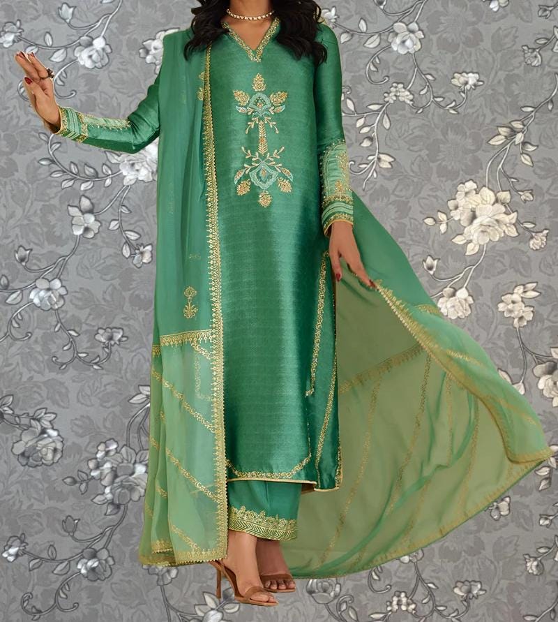 A woman wearing a long green dress with gold embroidery and a matching green shawl, standing against a gray floral background.