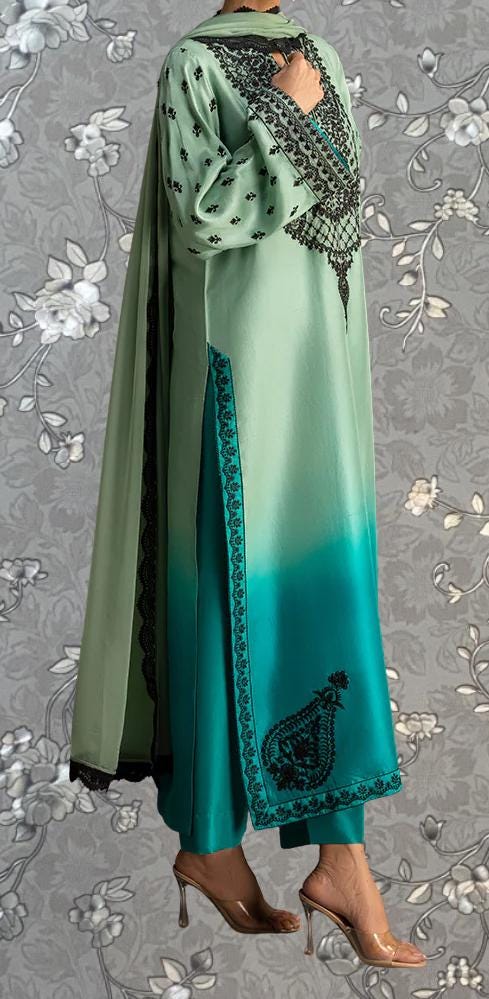 A person wearing a long, green and teal dress with intricate embroidery and a matching green and teal patterned shawl.