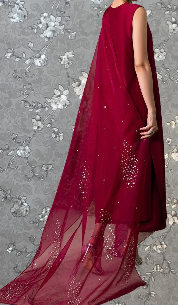 A person wearing a long, red dress with a sheer, flowing train and embellished with small white flowers.