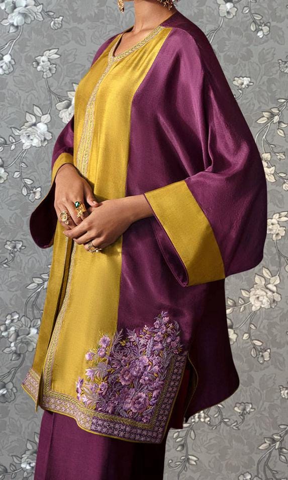 A person wearing a vibrant purple and gold dress with intricate embroidered patterns on the sleeves and hem.