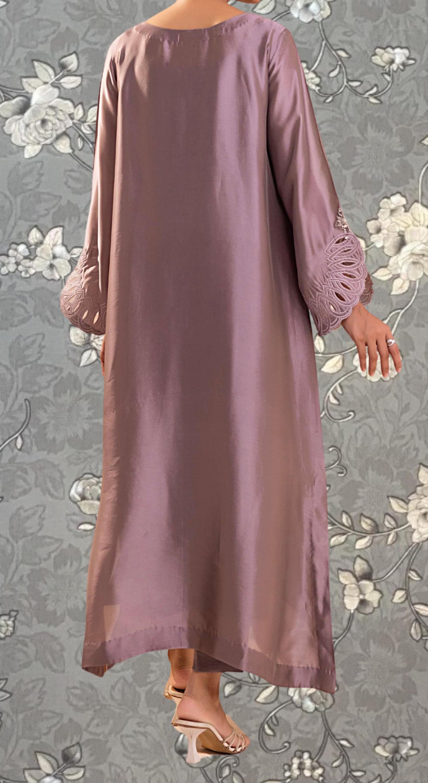 A person wearing a long, purple satin dress with lace sleeves stands against a floral background.