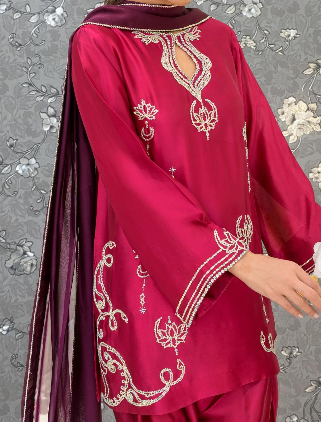 A person wearing a vibrant red and purple dress with intricate embroidered designs, including floral patterns and a central design element.