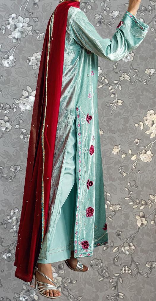 A person wearing a long, light blue dress with red accents, including a red shawl draped over the shoulders. The dress has a floral pattern on the skirt and the sleeves, and the person is wearing silver high heels.