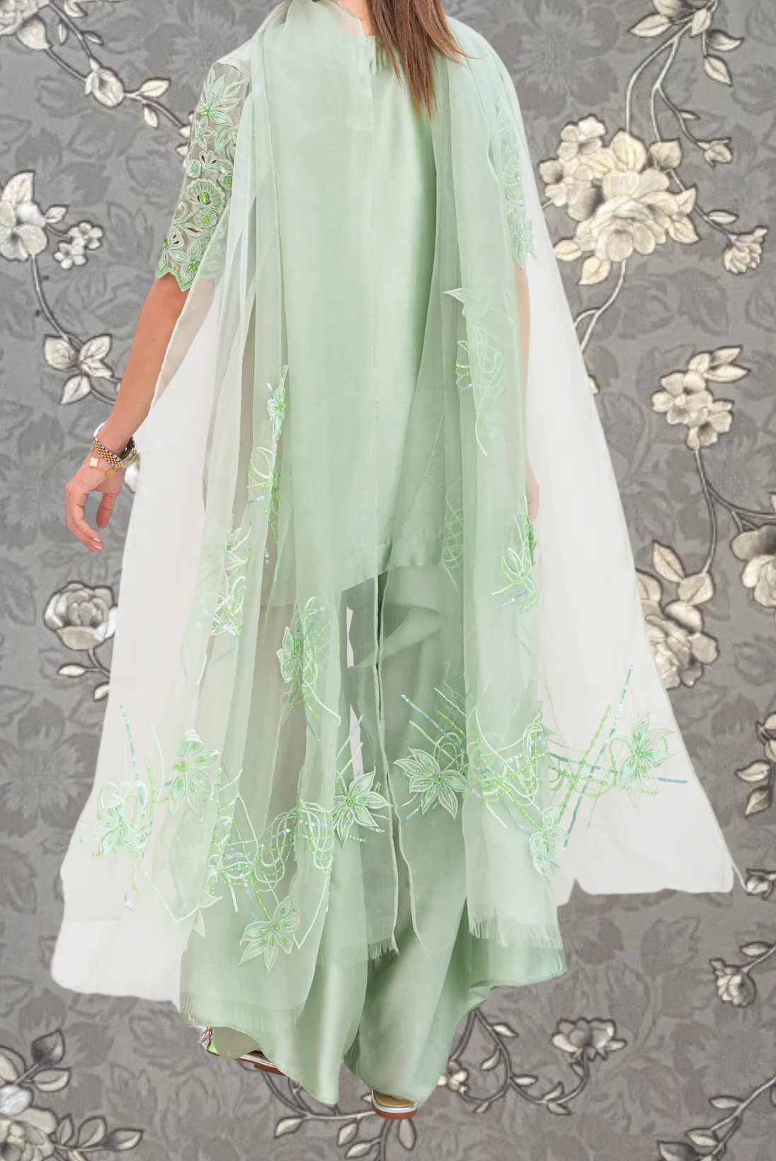A person wearing a long, flowing green dress with intricate embroidered designs on the sleeves and back.