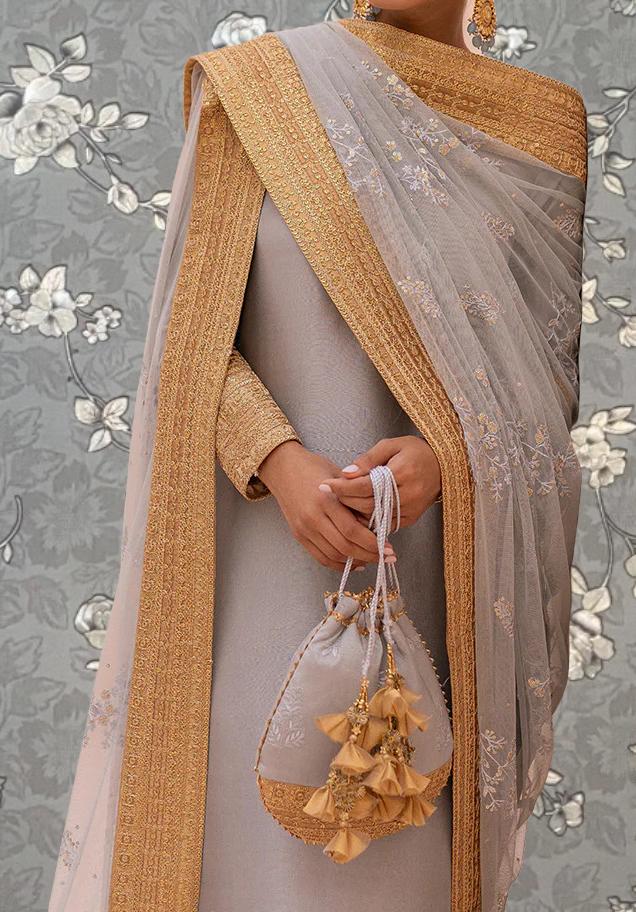 A person wearing a gray and gold dress with a gold and white patterned shawl, holding a small purse with gold tassels.