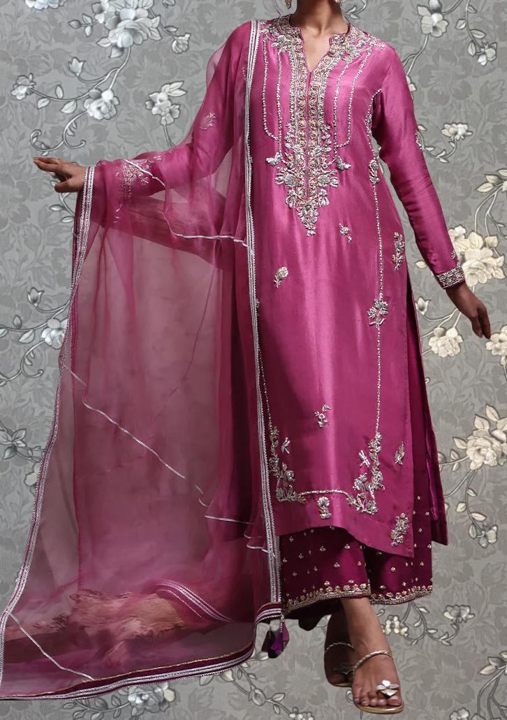 A woman wearing a long, pink dress with intricate embroidery and a matching shawl.