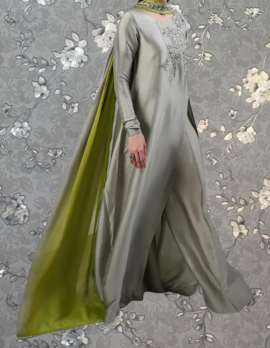 A person wearing a long, flowing gray dress with a green cape-like garment draped over the shoulder.
