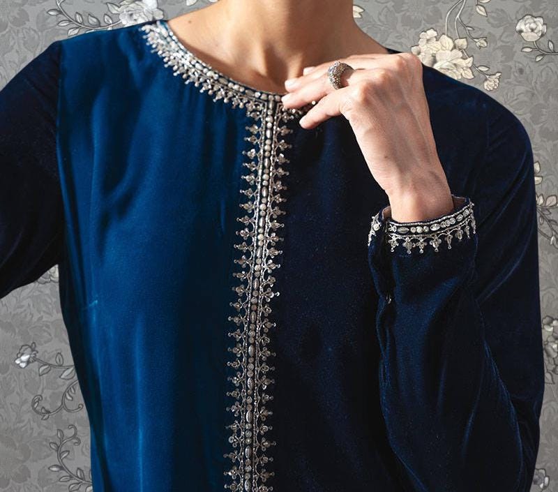 A close-up of a person wearing a blue velvet dress with a silver embroidered design on the collar and sleeves.