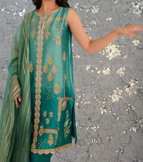 A woman wearing a green and gold dress with intricate embroidery stands against a gray floral background.